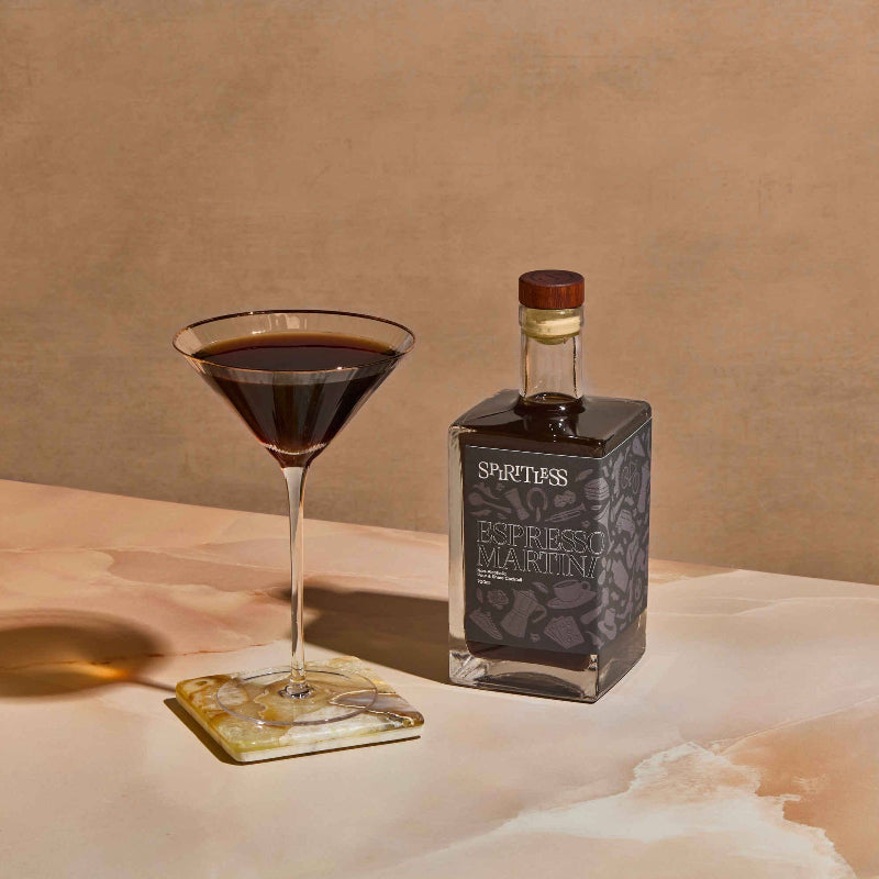 Bottle of Spirtless and a cocktail glass with dark liquid on a textured surface.